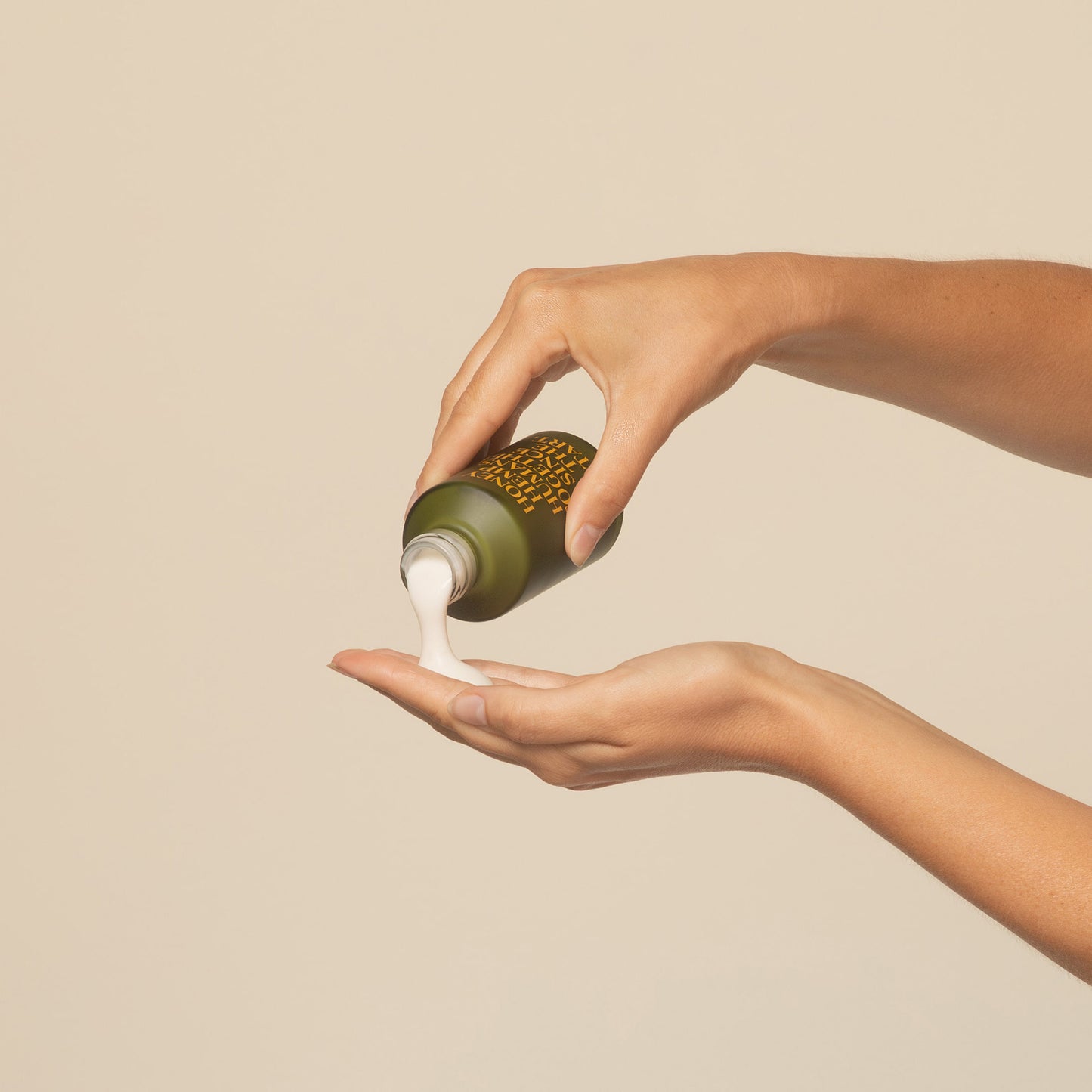 hands puring apo ge manuka honey skincare clarifying milk cleanse from 120ml glas bottle on a beige background