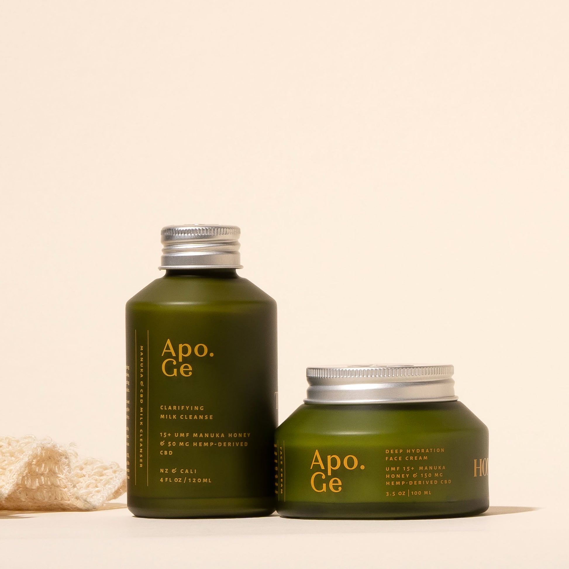 apo ge manuka honey skincare products clarifying milk cleanse and deep hydration face cream with silver lids on a beige background