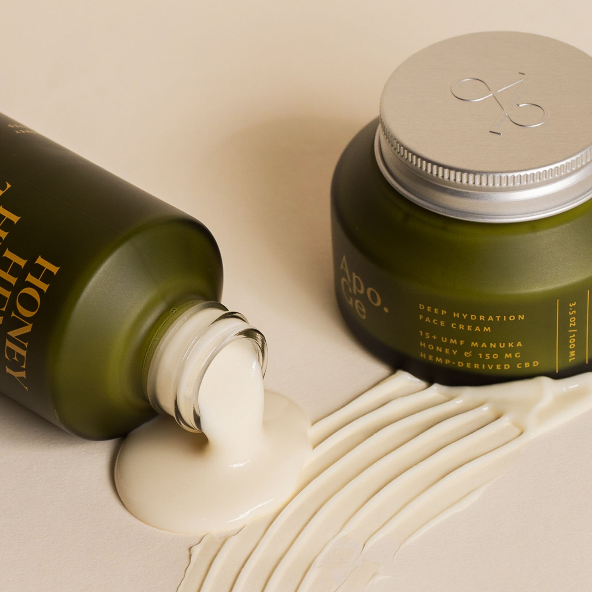 apo ge manuka honeyu skincare clarifying milk cleanse and deep hydration face cream spilling product on a beige background