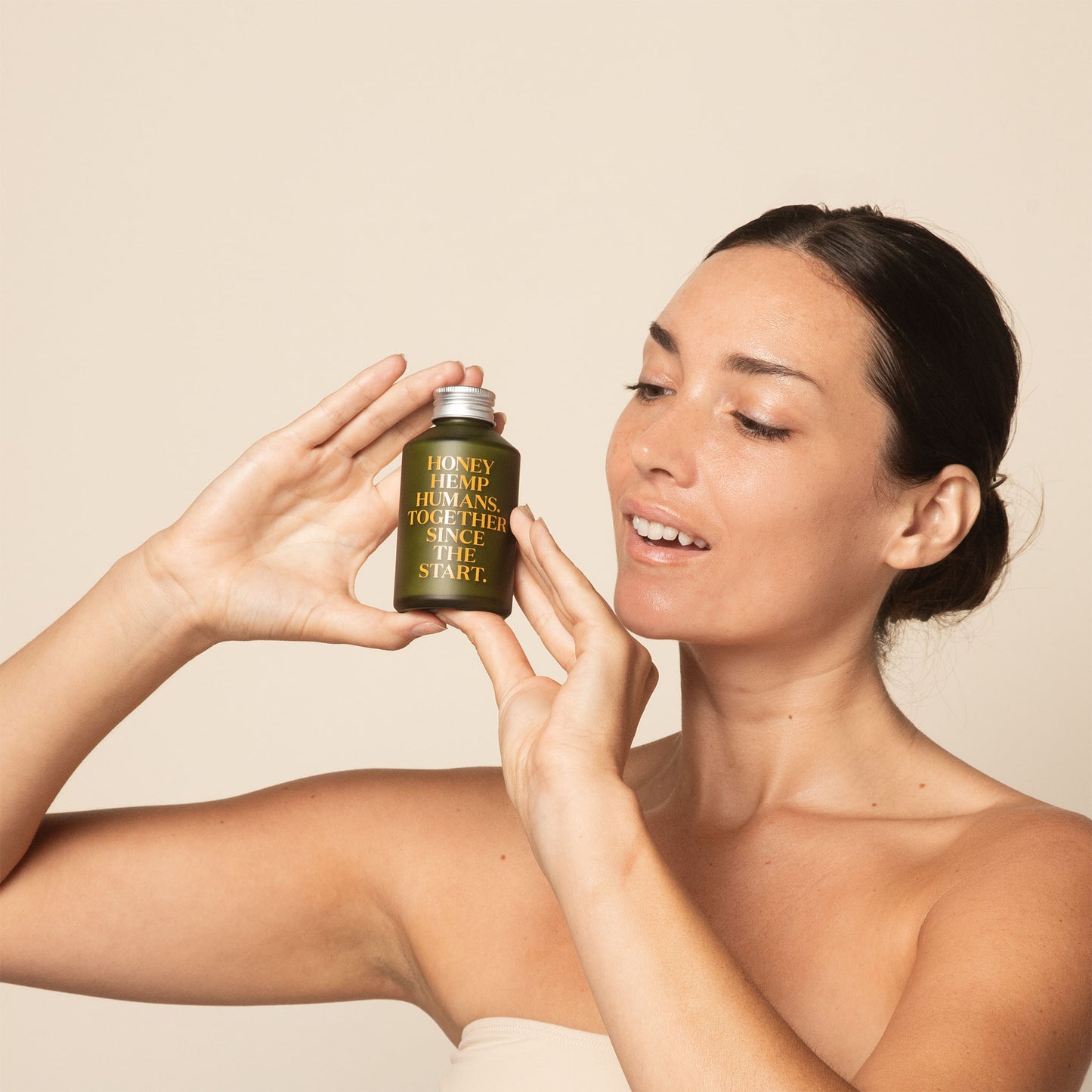 woman holding 120ml green glass bottle containing apo ge manuka honey skincare clarifying milk cleanse infront of a beige background
