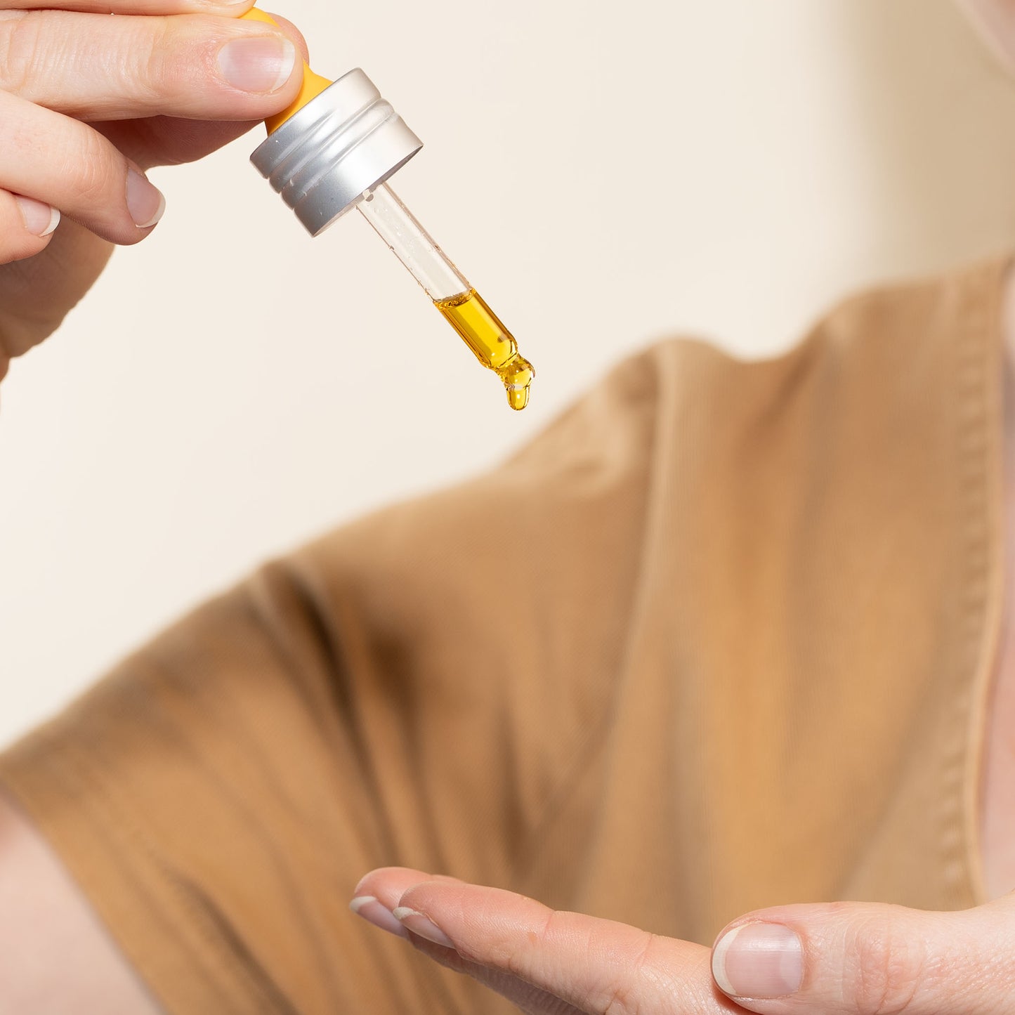 Person holding ape ge manuka honey skincare renewing night elixer dropper with liquid over their palm against a neutral background