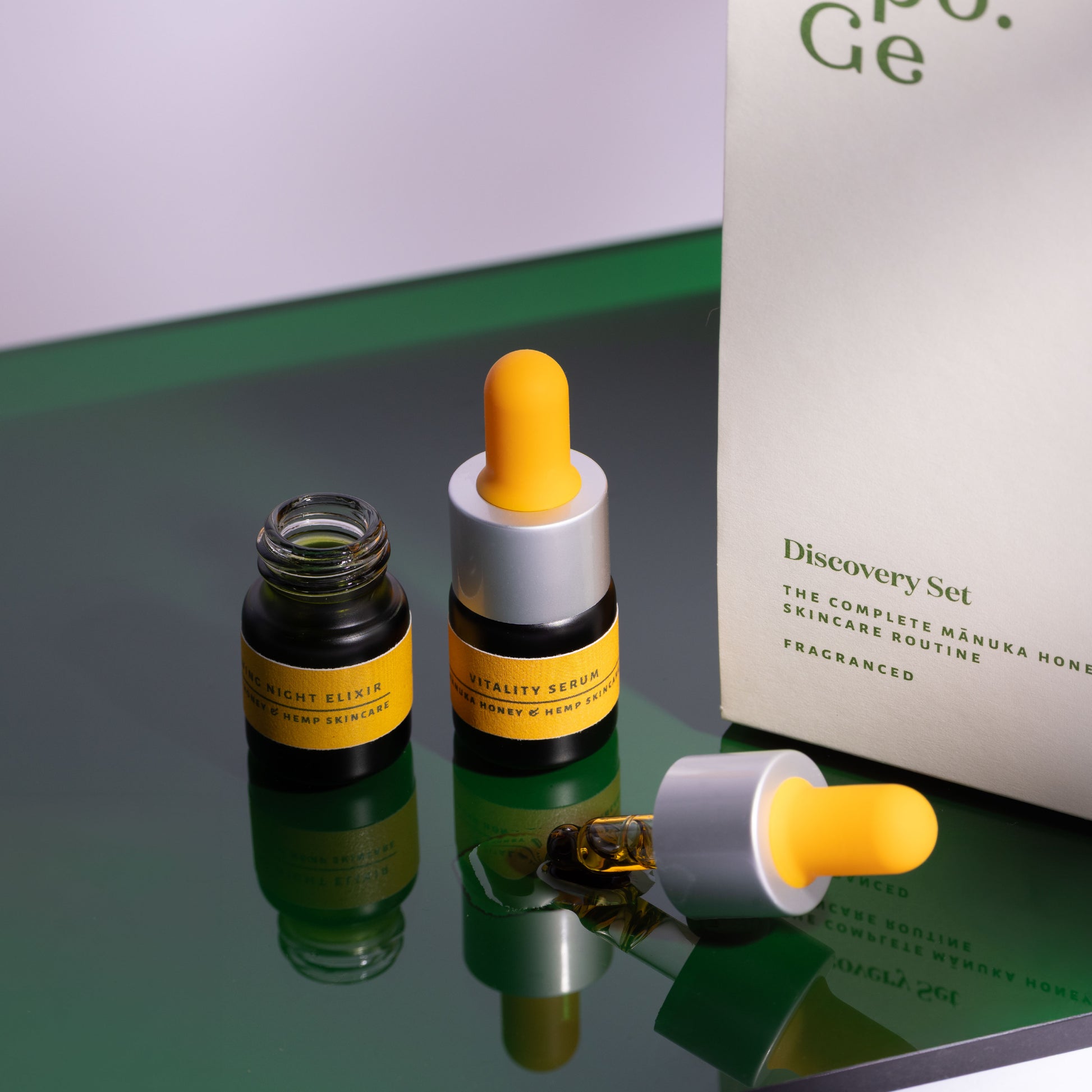 Two skincare mini bottles with yellow caps on a reflective surface, next to a Apo.Ge Discovery Set box.