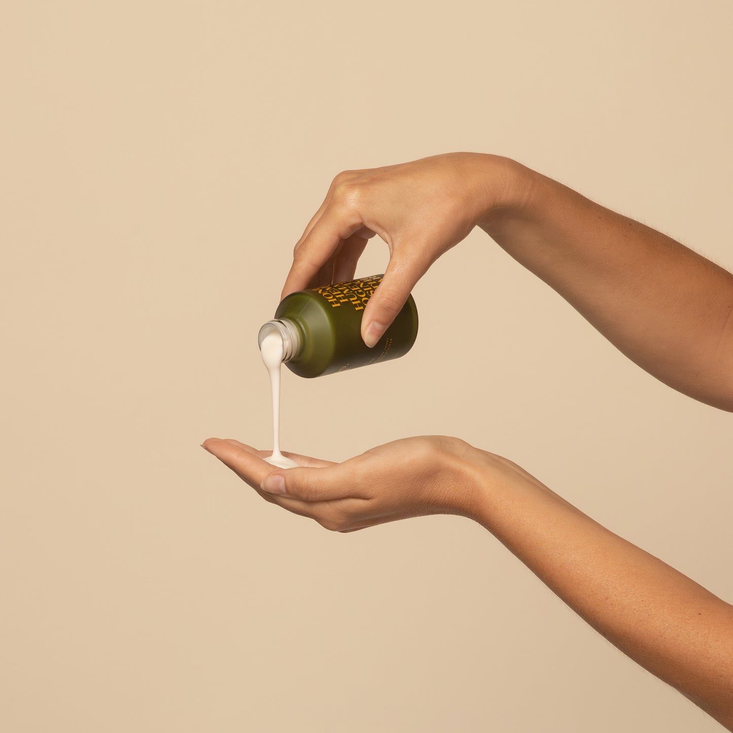 female models hand pouring a apo ge manuka honey skincare clarifying milk cleanse from a 120ml green bottle onto another hand against a beige background