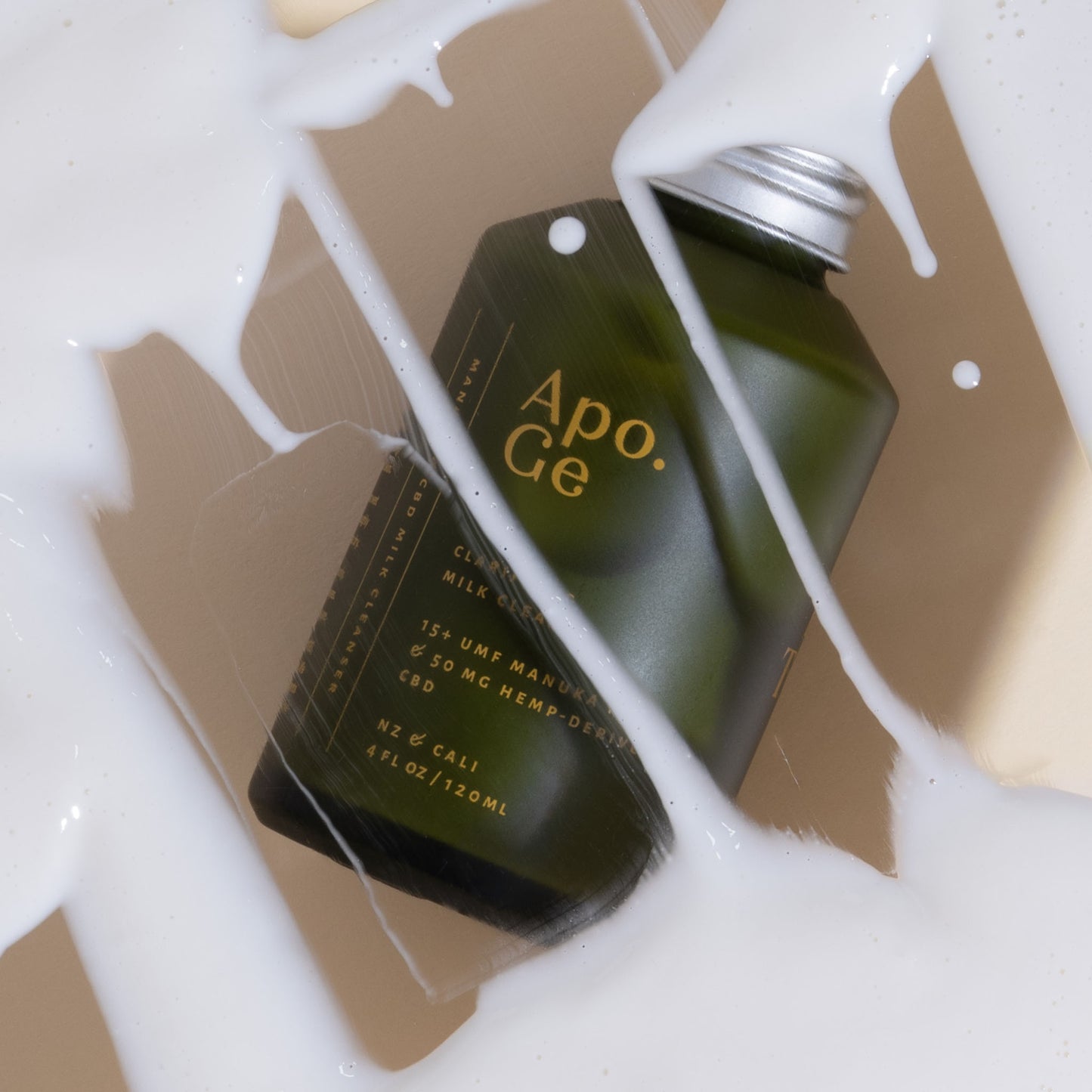 120ml green glass bottle with 'Apo.Ge' branding on a white background and apo ge manuka honey skincare clarifying milk cleanse spilled on background 