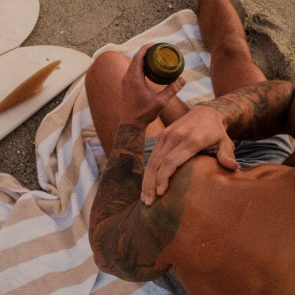 Male model applying Apo.Ge botanical relief balm arnica balm to shoulder on beach