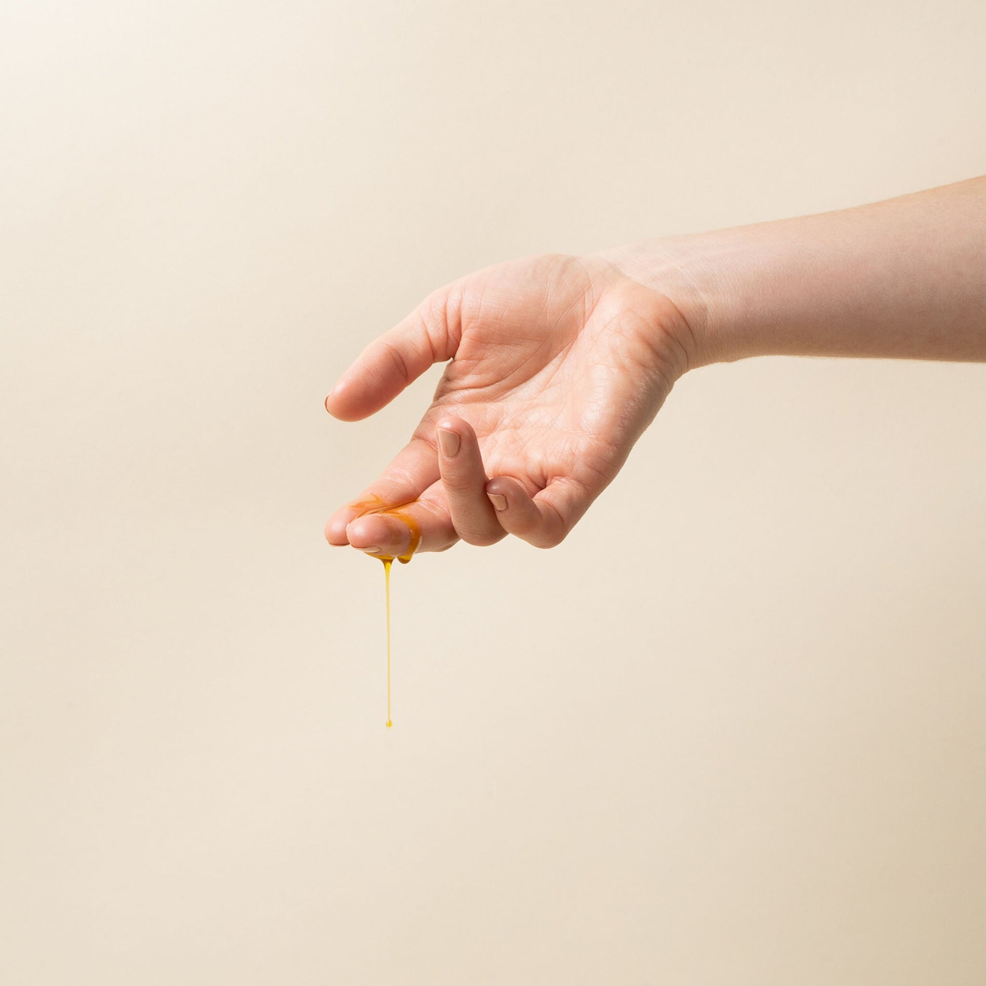 Hand dripping with apo ge manuka honey sincare renewing night elixer against a beige background