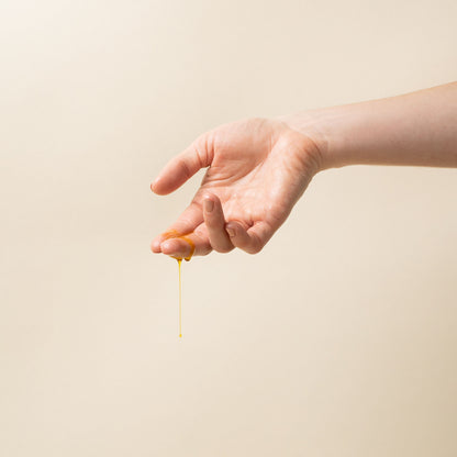 Hand dripping with apo ge manuka honey sincare renewing night elixer against a beige background