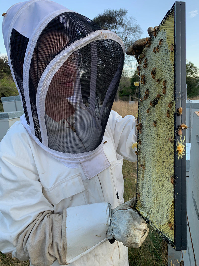 Apo.Ge founder Colleen in a bee suit holding a frame of manuka honey in New Zealand