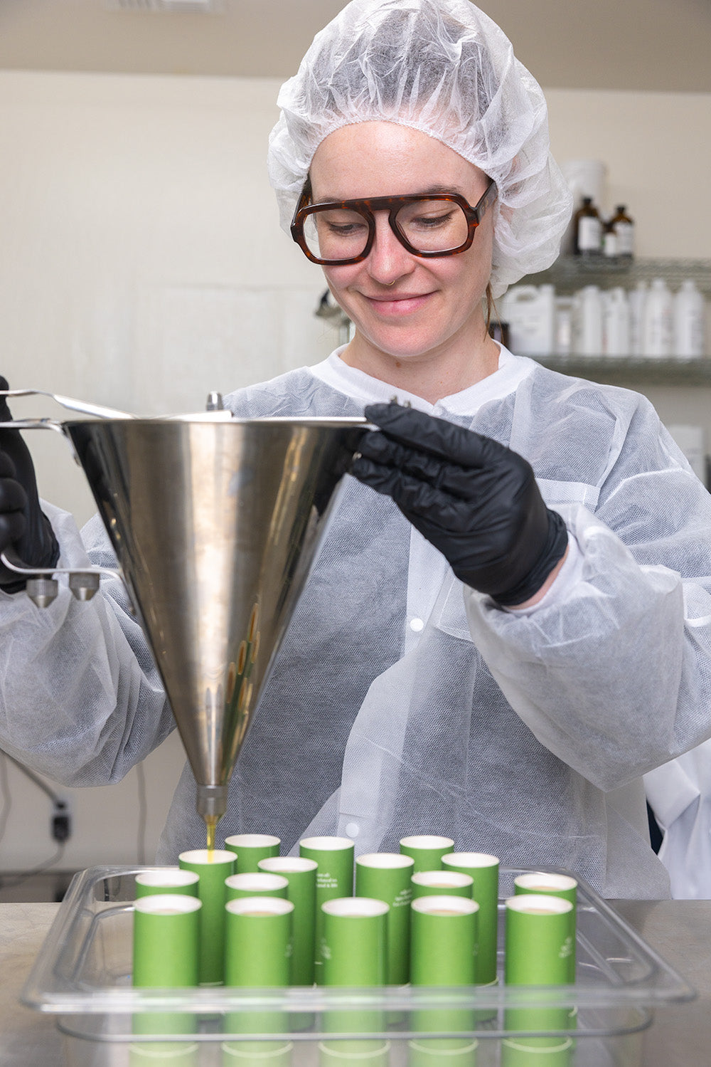 Apo.Ge founder and formulator Colleen in a lab setting with a funnel and green containers